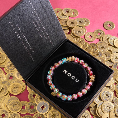 Golden Snake Firework Glass Rose Bracelet with glowing beads and 18k gold plated snake charm in black box surrounded by gold coins by NOGU